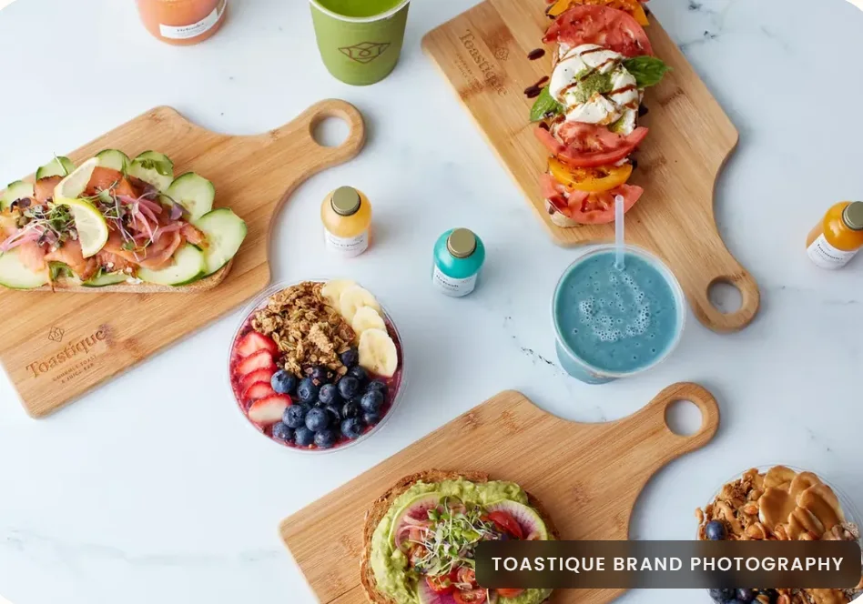 Toastique toasts, smoothie bowls and juices arranged on wooden serving boards
